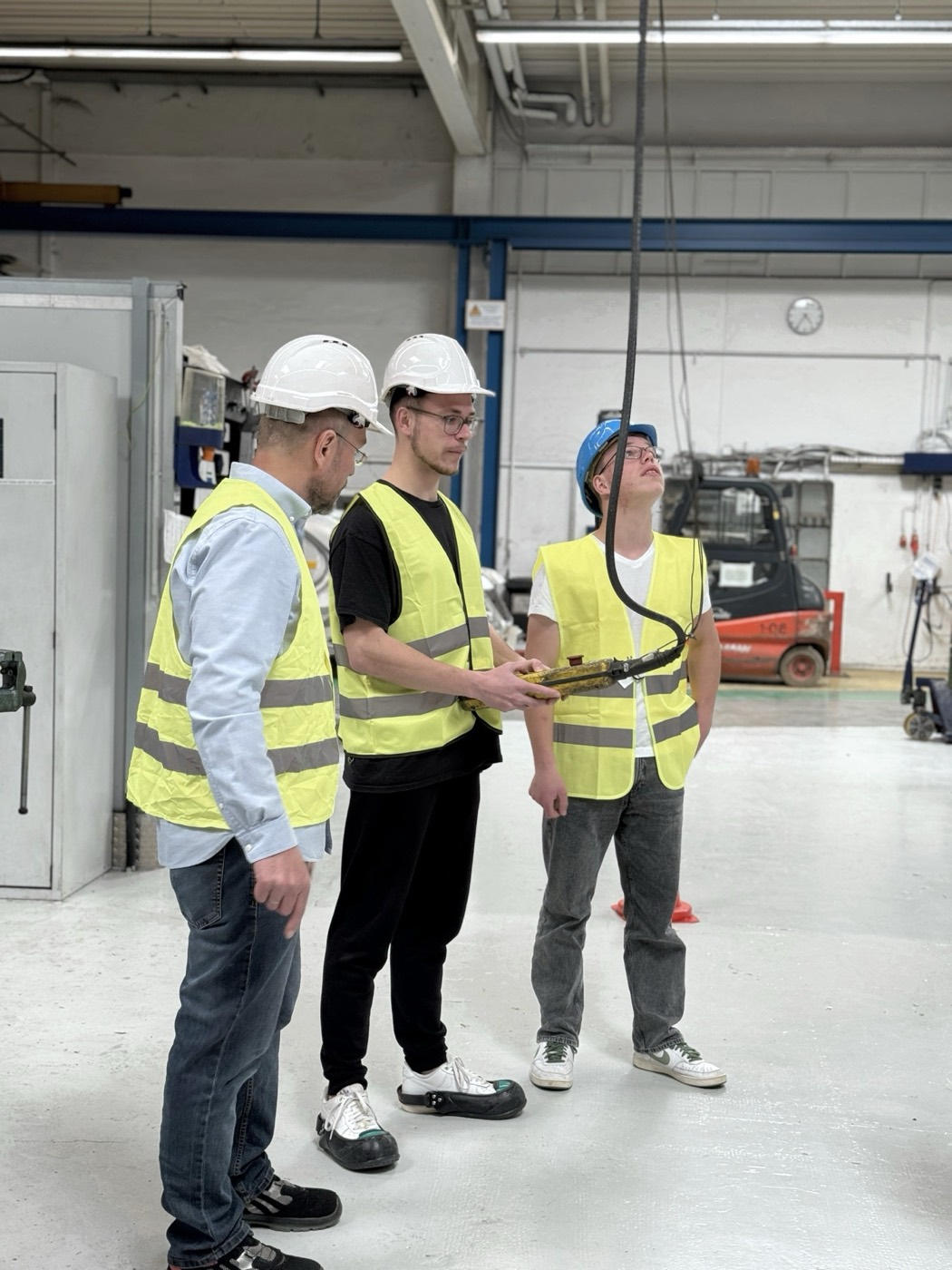 Drei Teilnehmer mit Helm und Warnweste in der Schulungshalle